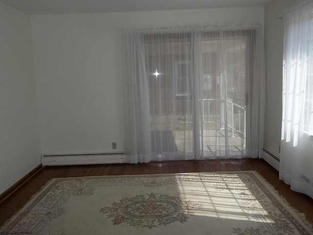 spare room featuring a baseboard heating unit, a healthy amount of sunlight, and wood finished floors