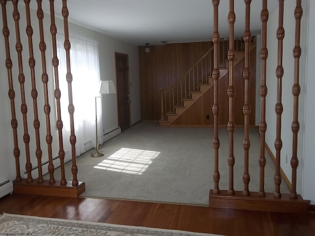 interior space with stairway, wooden walls, wood finished floors, and baseboard heating