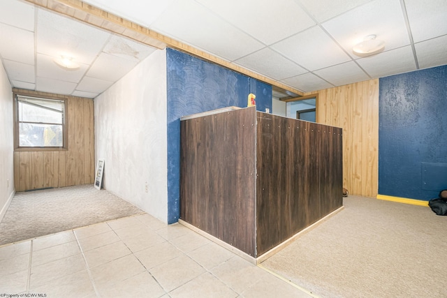 carpeted empty room with tile patterned floors, a paneled ceiling, and wood walls