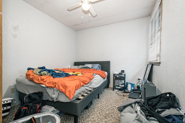 bedroom with ceiling fan, a textured ceiling, carpet, and a textured wall