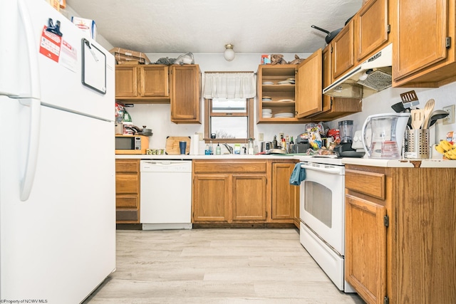 kitchen with white appliances, a sink, light countertops, light wood-style floors, and under cabinet range hood