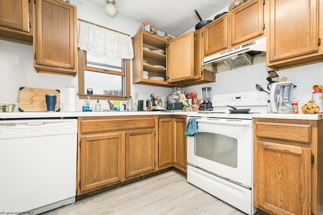 kitchen featuring under cabinet range hood, light countertops, brown cabinets, light wood-style floors, and white appliances