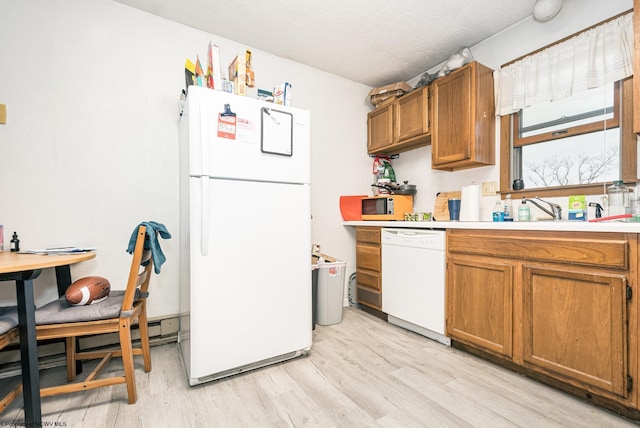 kitchen featuring light countertops, light wood-style flooring, brown cabinets, white appliances, and a sink