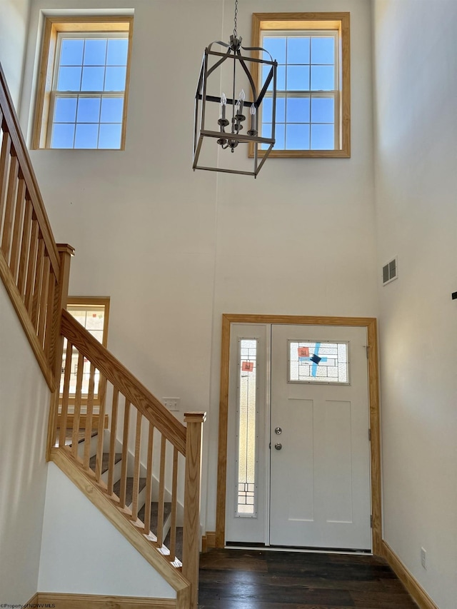 foyer entrance featuring visible vents, a notable chandelier, stairway, a towering ceiling, and dark wood-style flooring