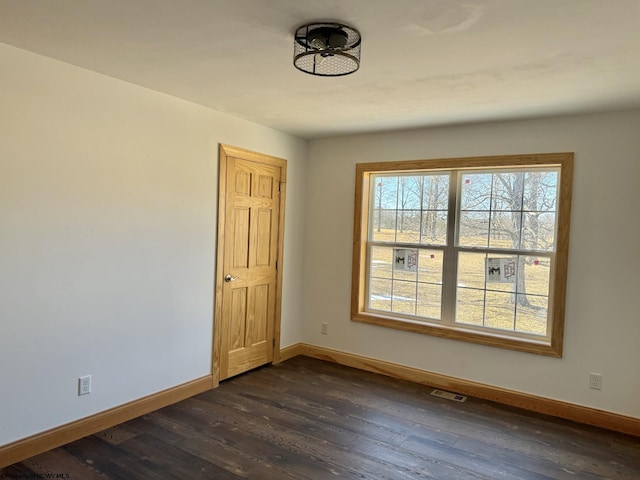 empty room with dark wood finished floors, visible vents, and baseboards