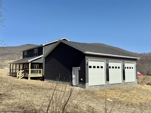 view of side of home with a mountain view, a shingled roof, driveway, and a garage