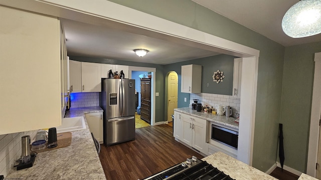 kitchen with white cabinets, dark wood-style floors, arched walkways, and appliances with stainless steel finishes