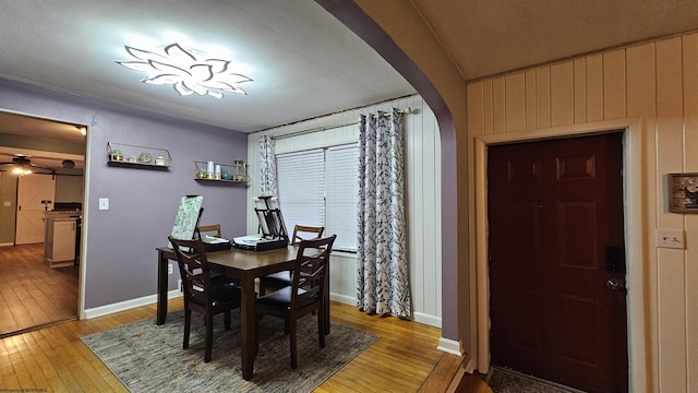 dining space featuring baseboards, arched walkways, and light wood-style floors