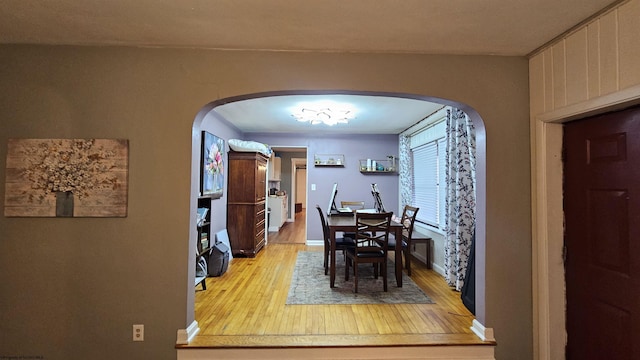 dining space featuring light wood-style flooring, baseboards, and arched walkways