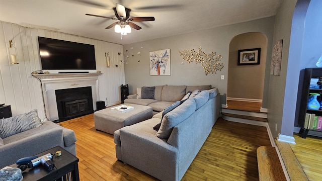 living area with a fireplace with flush hearth, wood-type flooring, arched walkways, and a ceiling fan