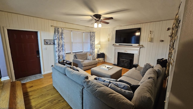 living area featuring a fireplace with flush hearth, baseboards, light wood-style flooring, and a ceiling fan