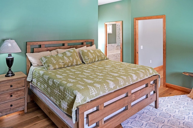 bedroom with ensuite bath, wood finished floors, and baseboards