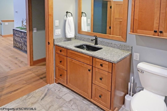 bathroom with toilet, vanity, baseboards, and wood finished floors