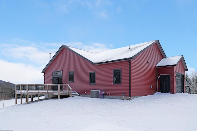 snow covered property featuring an attached garage, central AC, and a deck