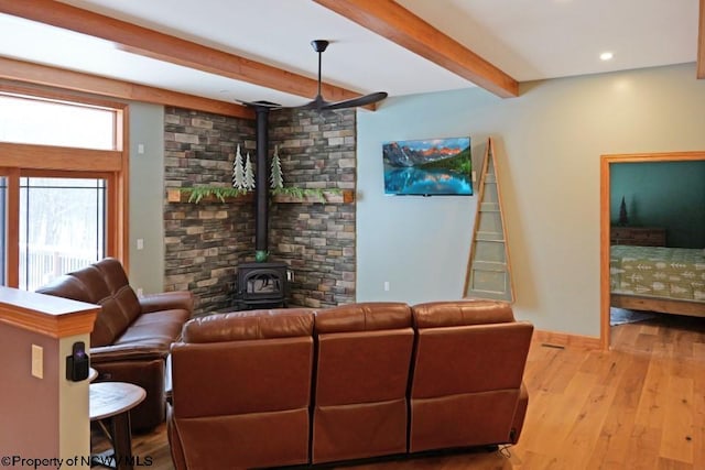 living room with baseboards, beam ceiling, recessed lighting, a wood stove, and wood finished floors