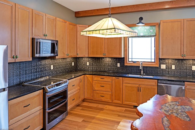 kitchen featuring pendant lighting, light wood-type flooring, decorative backsplash, stainless steel appliances, and a sink