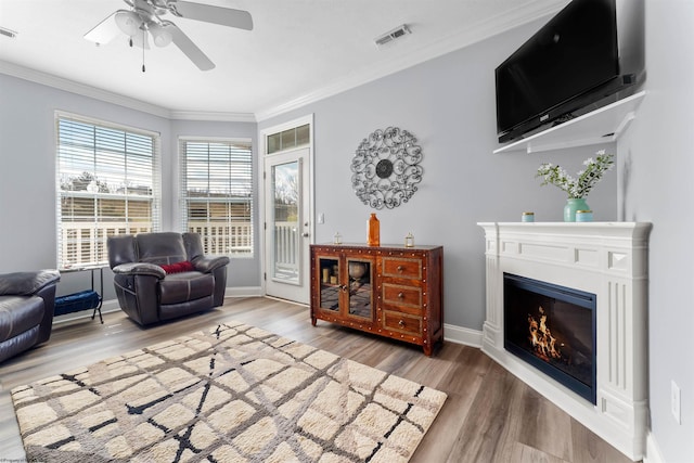 sitting room featuring wood finished floors, visible vents, a warm lit fireplace, and ornamental molding