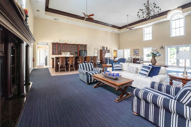 carpeted living area featuring a raised ceiling, a high ceiling, ornamental molding, and a ceiling fan