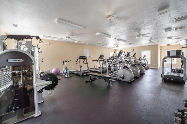 workout area with visible vents, a textured ceiling, baseboards, and a ceiling fan