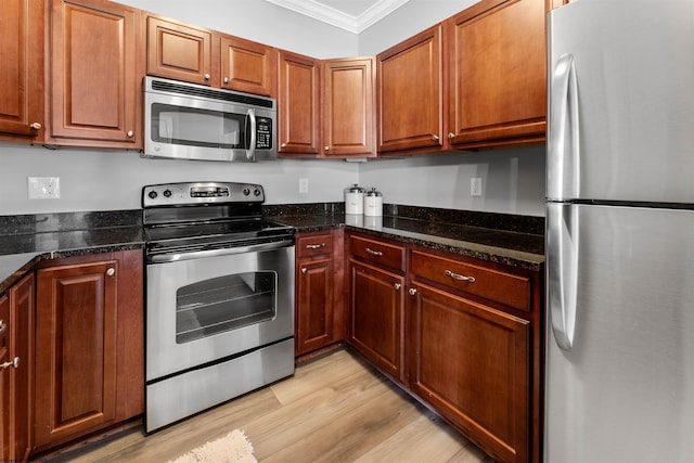 kitchen with crown molding, dark stone counters, appliances with stainless steel finishes, light wood-style floors, and brown cabinetry