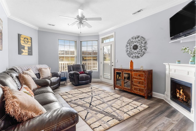 living area with visible vents, a warm lit fireplace, wood finished floors, and ornamental molding