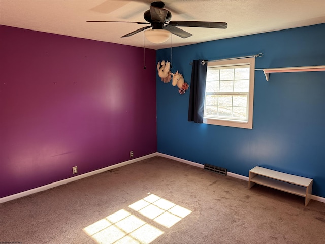 empty room with visible vents, a textured ceiling, carpet floors, baseboards, and ceiling fan