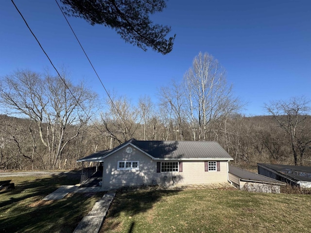 exterior space featuring a front lawn, a wooded view, and metal roof