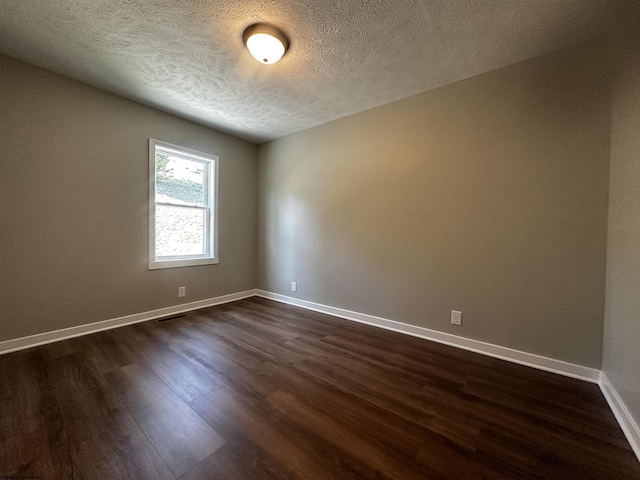 spare room with a textured ceiling, dark wood-type flooring, and baseboards