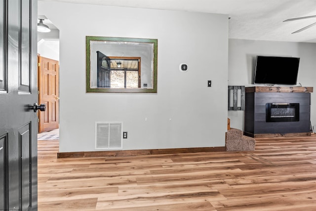 interior space featuring visible vents, wood finished floors, a ceiling fan, and a glass covered fireplace