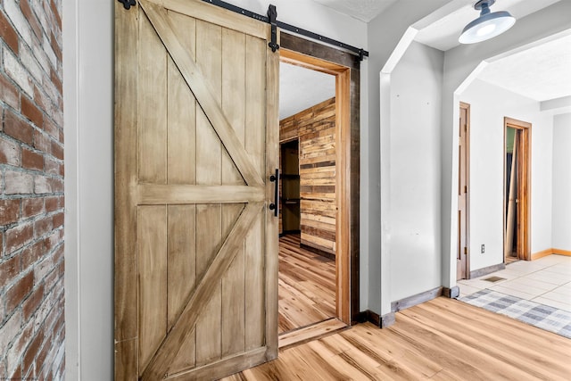 corridor featuring brick wall, baseboards, light wood-type flooring, a barn door, and arched walkways