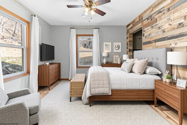 bedroom with an accent wall, baseboards, light wood-type flooring, and ceiling fan