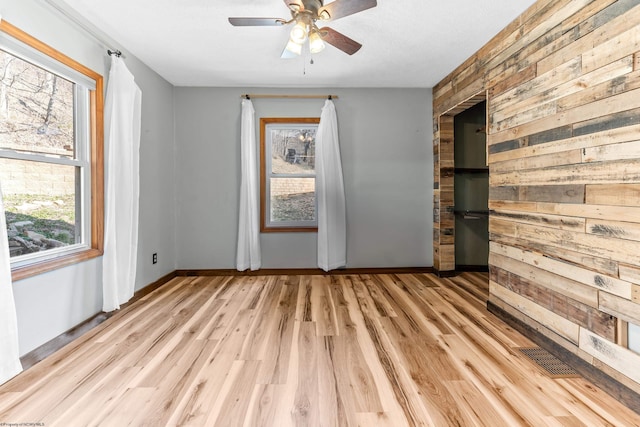 empty room with light wood-style flooring, wooden walls, baseboards, and ceiling fan