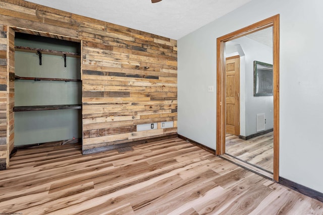 unfurnished bedroom featuring wooden walls, wood finished floors, visible vents, and baseboards