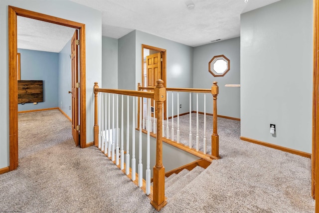 hall featuring baseboards, an upstairs landing, a textured ceiling, and carpet flooring