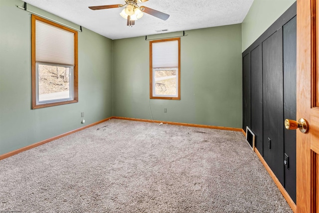 unfurnished bedroom with visible vents, multiple windows, a textured ceiling, and carpet flooring