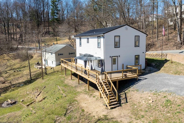 rear view of house featuring driveway, a wooden deck, and stairs