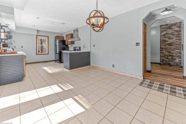 kitchen featuring freestanding refrigerator, a peninsula, wall chimney exhaust hood, light countertops, and light tile patterned floors