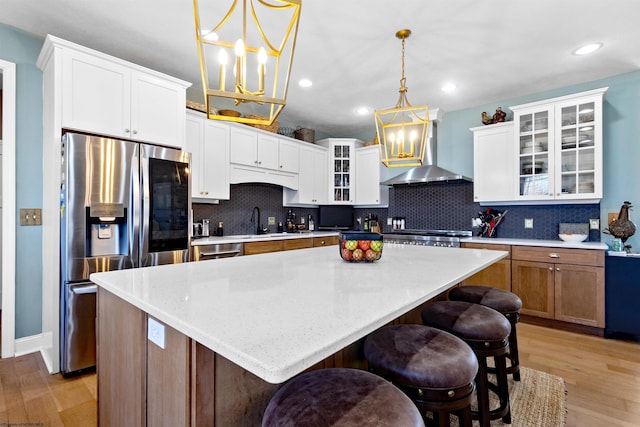 kitchen with a sink, decorative backsplash, light wood-style floors, wall chimney exhaust hood, and stainless steel fridge