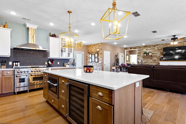 kitchen with visible vents, beverage cooler, white cabinetry, wall chimney exhaust hood, and range with two ovens