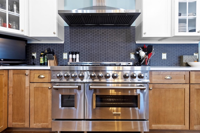 kitchen with double oven range, light countertops, glass insert cabinets, and wall chimney range hood