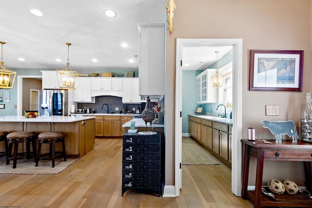 kitchen with a breakfast bar, light countertops, light wood-style flooring, stainless steel refrigerator with ice dispenser, and a sink