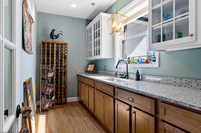 interior space featuring visible vents, a notable chandelier, a sink, light wood-style floors, and baseboards