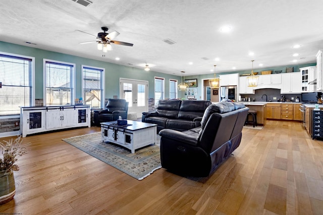 living area featuring visible vents, light wood-style flooring, recessed lighting, french doors, and a textured ceiling