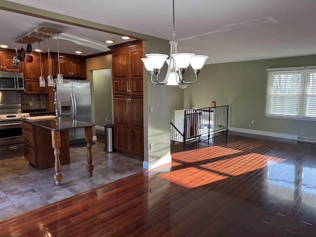 kitchen with wood finished floors, a breakfast bar, stainless steel appliances, decorative backsplash, and a chandelier