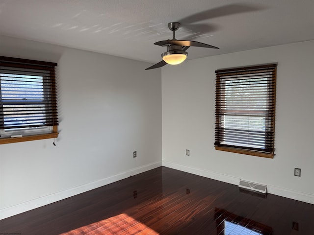 spare room with a ceiling fan, dark wood-type flooring, visible vents, and baseboards