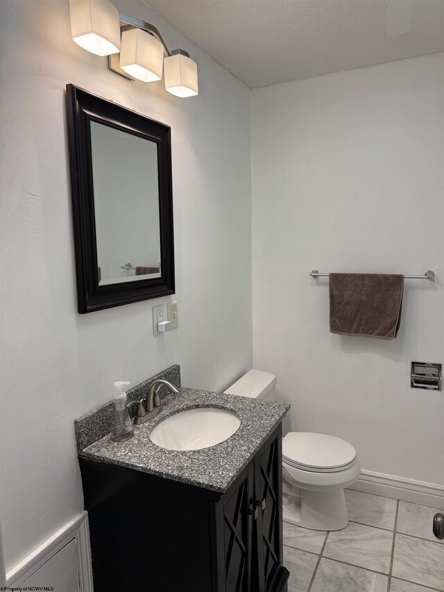 half bathroom featuring baseboards, toilet, marble finish floor, and vanity