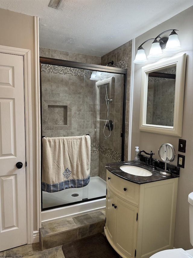 bathroom featuring a shower stall, a textured ceiling, vanity, and toilet