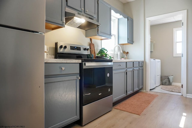 kitchen with stainless steel electric range oven, gray cabinets, freestanding refrigerator, under cabinet range hood, and washing machine and dryer