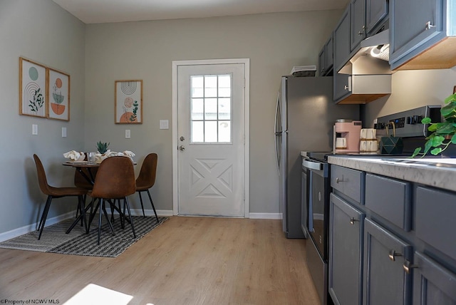 kitchen with light wood-type flooring, gray cabinetry, under cabinet range hood, light countertops, and baseboards