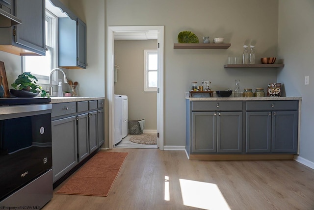 kitchen featuring light wood-type flooring, gray cabinetry, under cabinet range hood, open shelves, and a sink